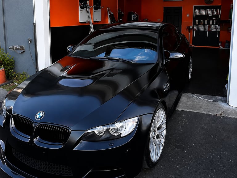 Black BMW coupe parked in a garage with orange and red walls, hood open to show blue engine cover