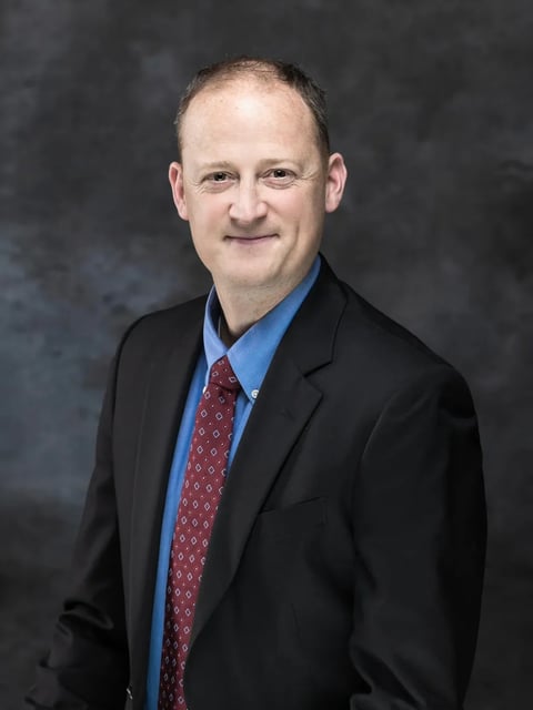 Professional headshot of Michael P. Owsiak in a black blazer, blue shirt, and red patterned tie