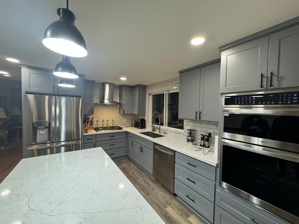 Modern kitchen with gray cabinets, marble countertop, stainless steel appliances, and pendant lighting