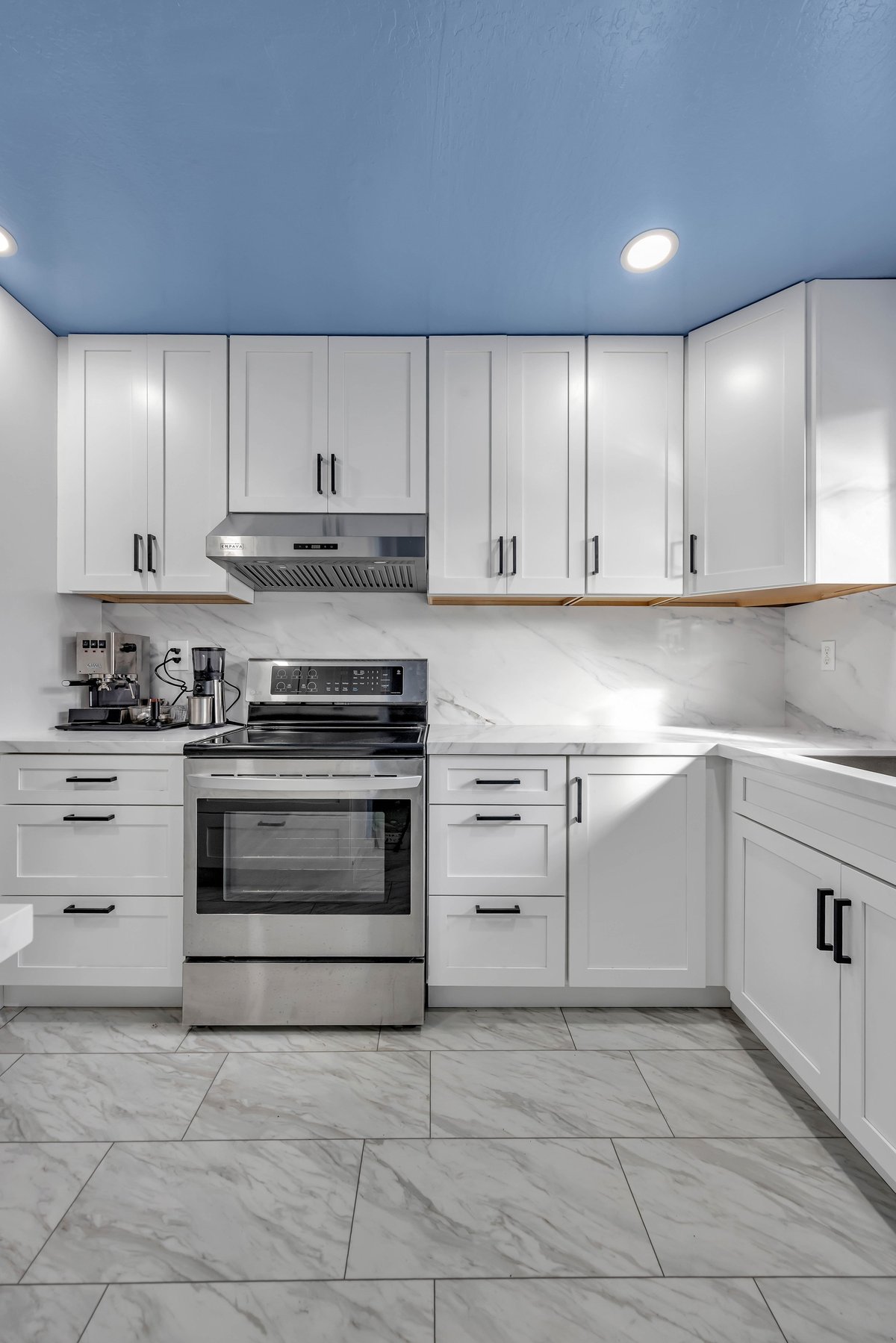 Modern kitchen with white cabinetry, stainless steel appliances, marble tile floor, and blue ceiling