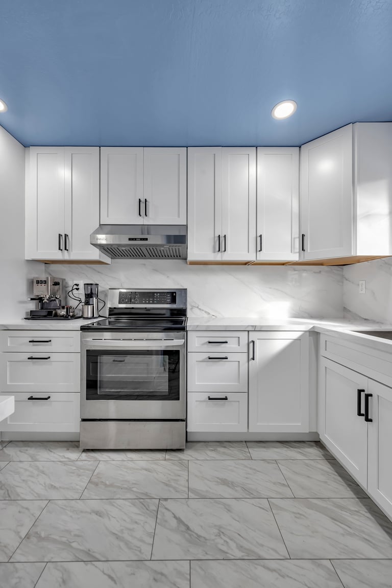 Modern kitchen with white cabinetry, stainless steel appliances, marble tile floor, and blue ceiling