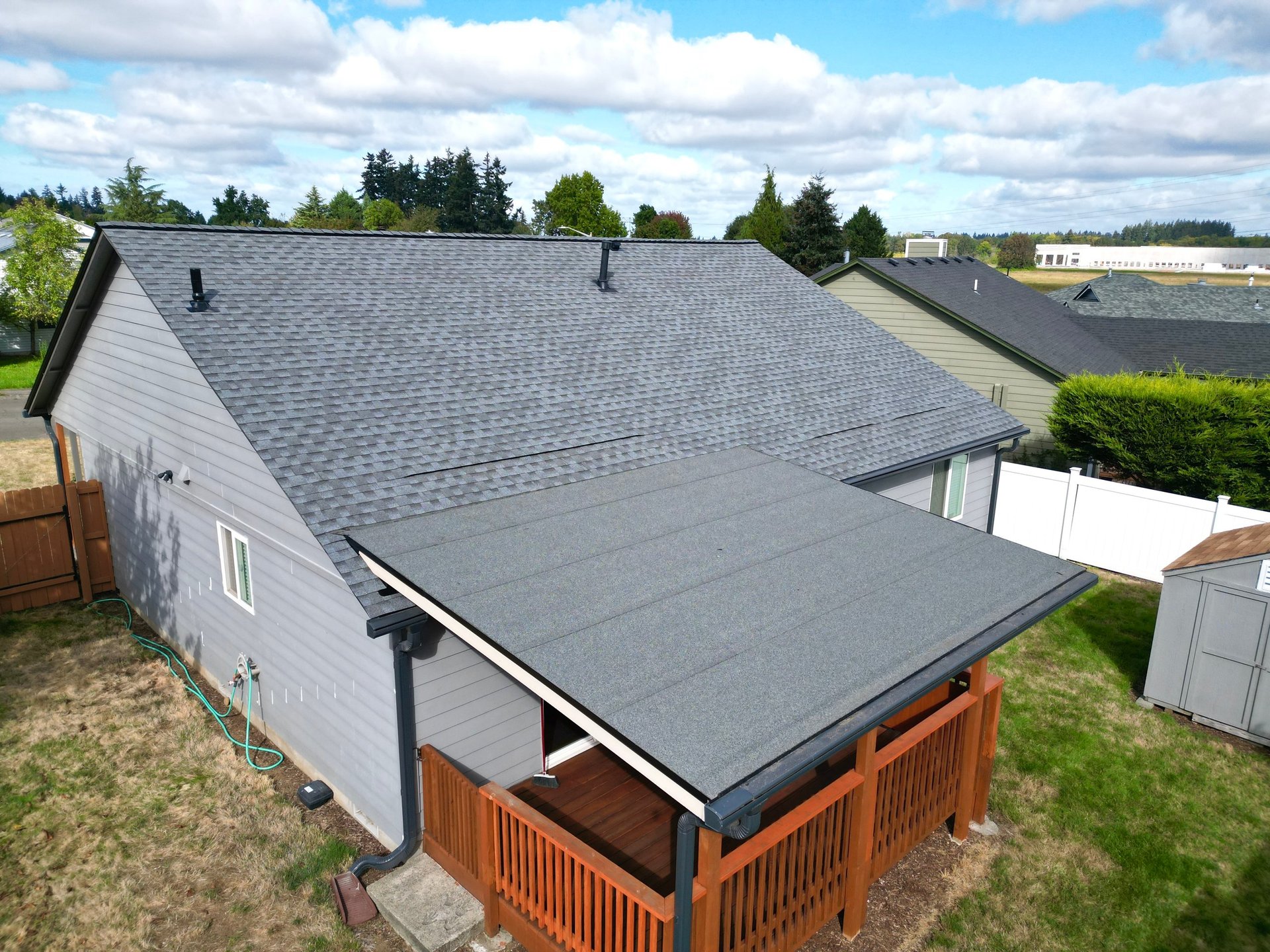 Aerial view of a residential property with roof, solar panels, and a wooden patio cover surrounded by trees