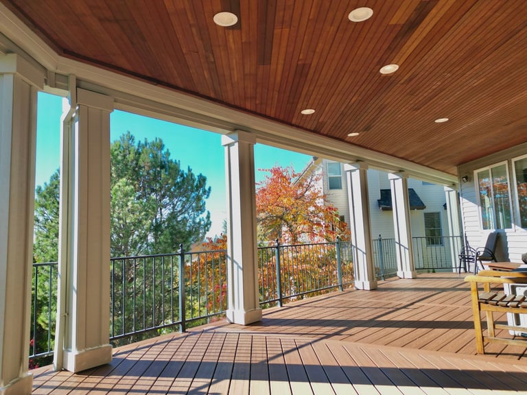 Modern covered deck with wooden ceiling, metal railings, and views of trees and mountains on a sunny day