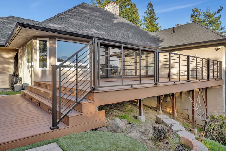 Modern home exterior with composite deck, metal railing, and glass sliding doors under clear sky with pine trees