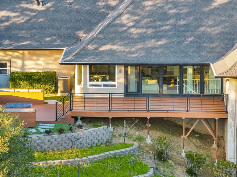 Aerial view of a modern house with an elevated wooden deck, large windows, and landscaped gardens below