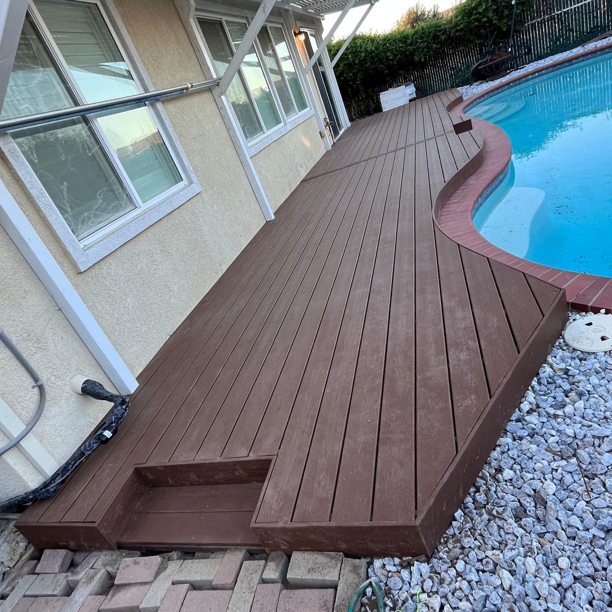 Dark brown composite deck with built-in seating and planter boxes by pool