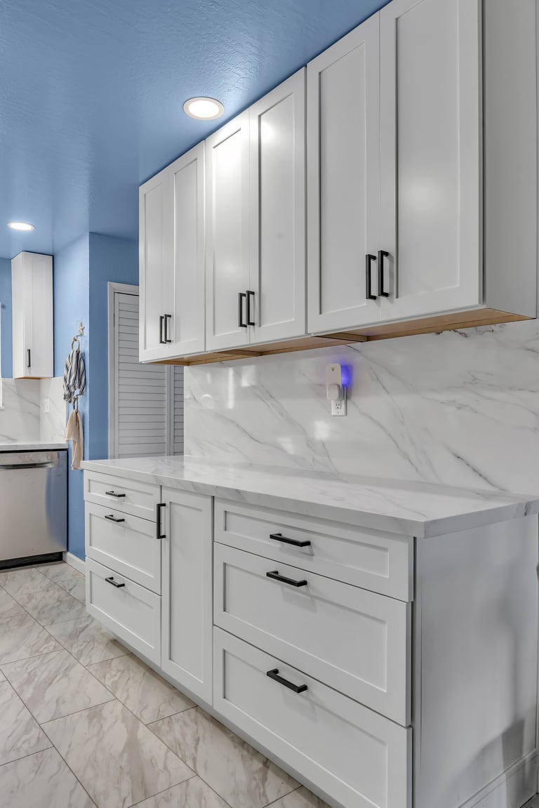 Modern kitchen with white cabinetry, marble countertop, blue walls, and recessed ceiling lights