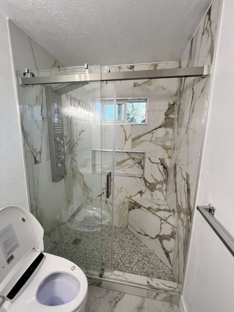 Modern marble-pattern tiled shower with glass doors and chrome fixtures
