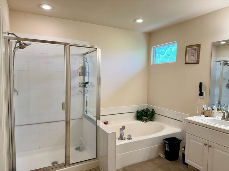 Dated bathroom with glass shower enclosure and white bathtub