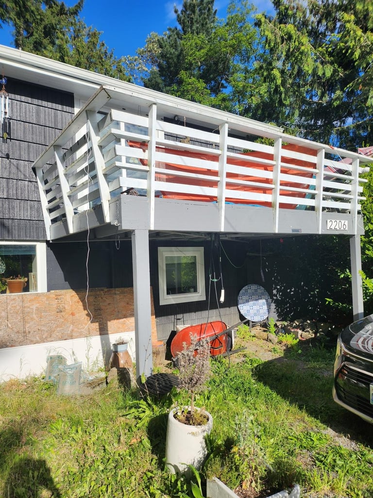 Small elevated deck with peeling white paint and solid railing blocking the view, attached to a dark-sided home
