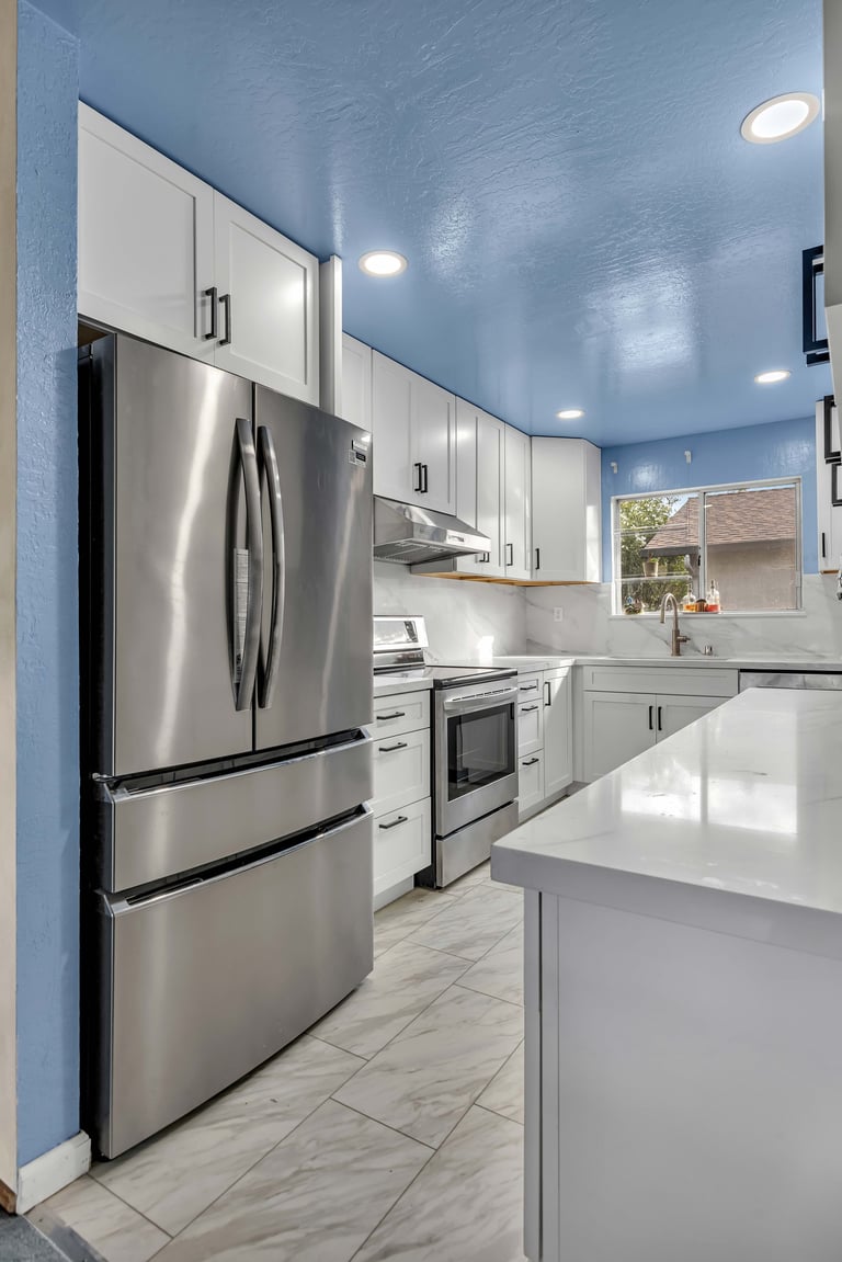 Modern kitchen with blue ceiling, white cabinets, stainless steel appliances, and marble tile flooring