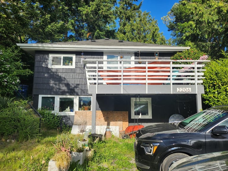 Two-story house with weathered small balcony and overgrown lawn, before deck replacement