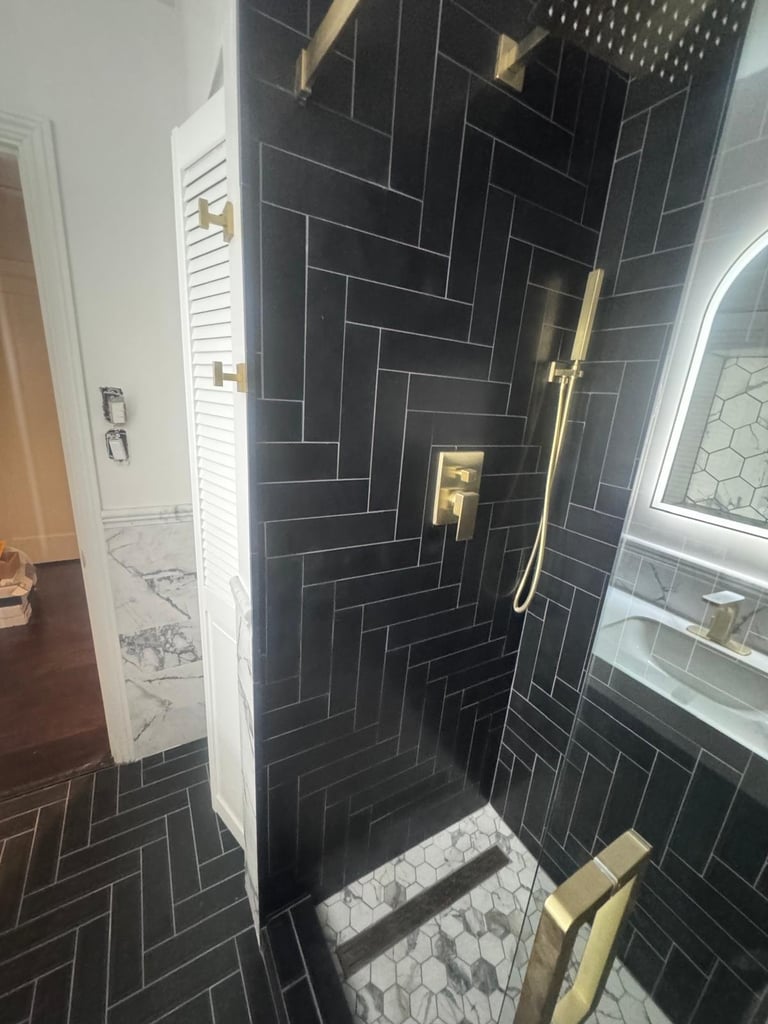 Black herringbone tile shower with brass fixtures and marble hex floor