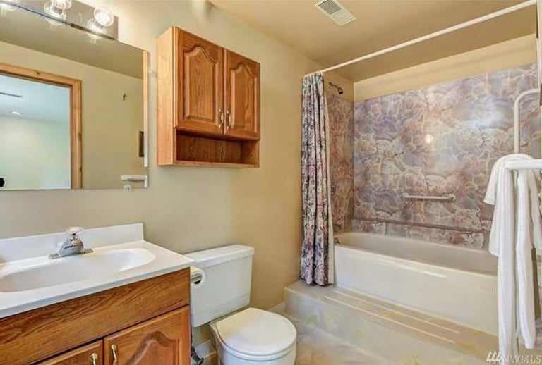 Dated bathroom with oak vanity and patterned shower curtain