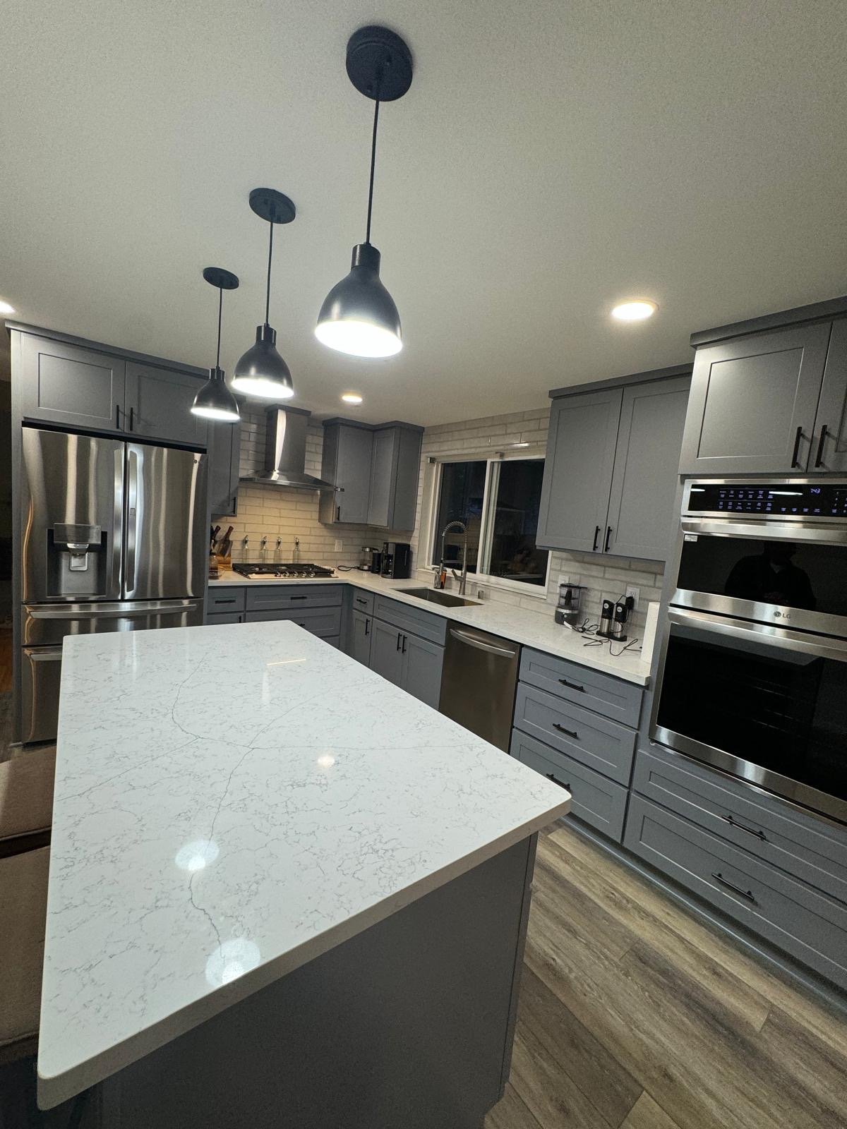 Modern kitchen with gray cabinets, white marble island, stainless steel appliances, and pendant lights overhead
