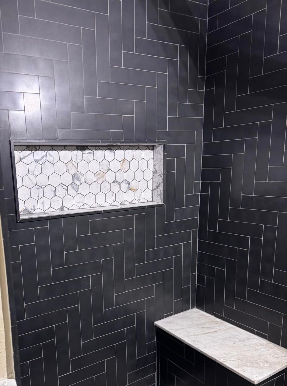 Modern shower with black herringbone tiles, white hexagonal niche, and marble bench