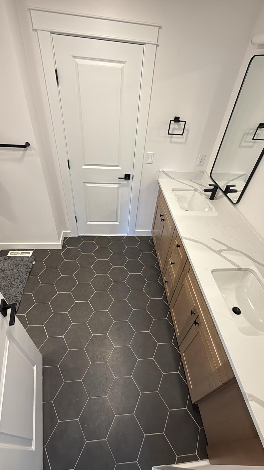Modern bathroom with gray hexagonal tile flooring, wood vanity, and black fixtures