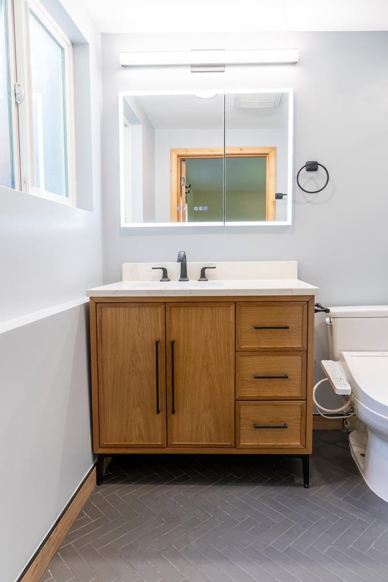 Modern bathroom with wooden vanity, marble countertop, and gray herringbone floor