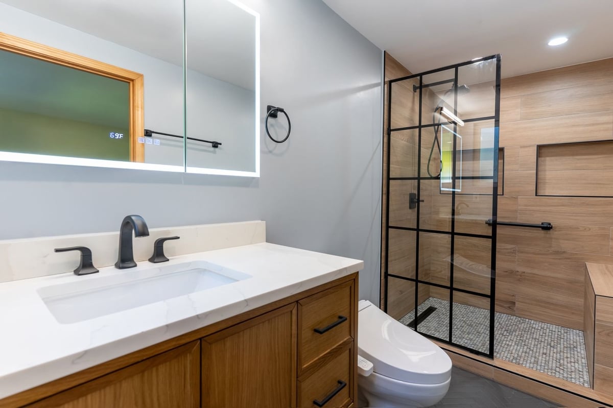 Modern bathroom with wood vanity, white countertop, and black-framed glass shower