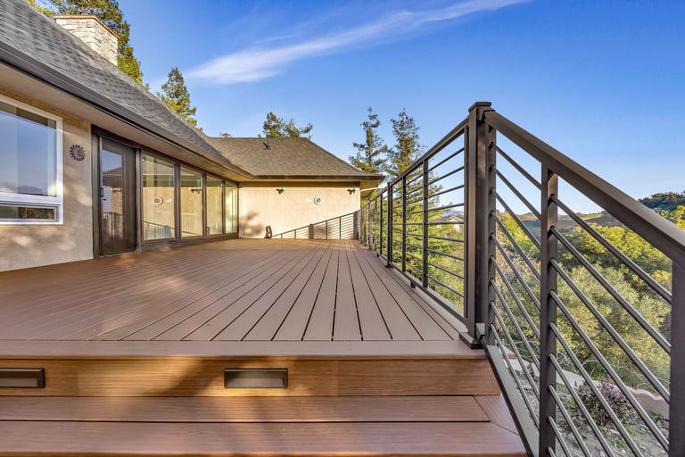 Modern wooden deck with cable railing overlooking a contemporary home and forested landscape under clear blue sky