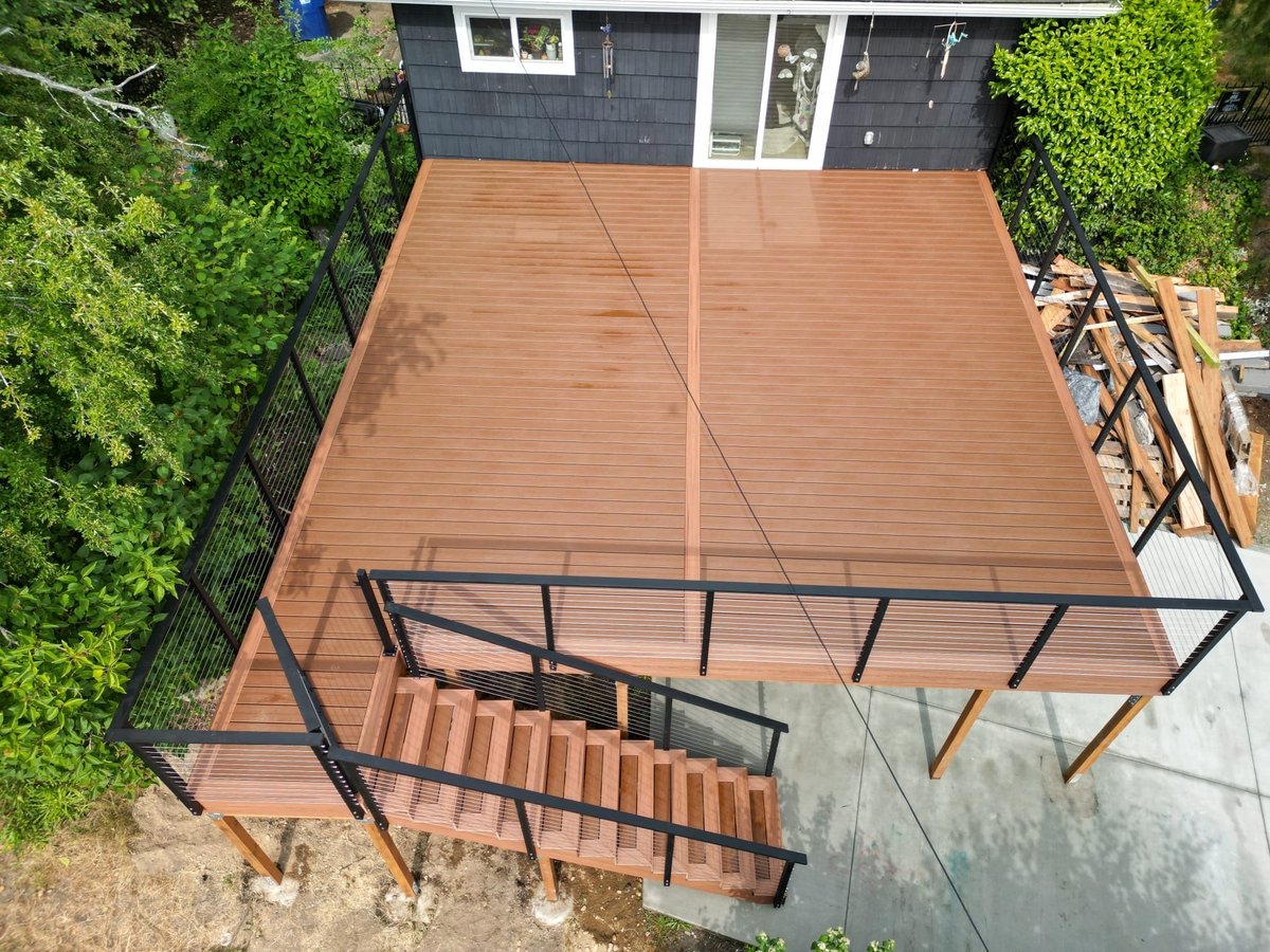 Aerial view of new elevated composite deck with black metal pergola and matching staircase leading to manicured lawn
