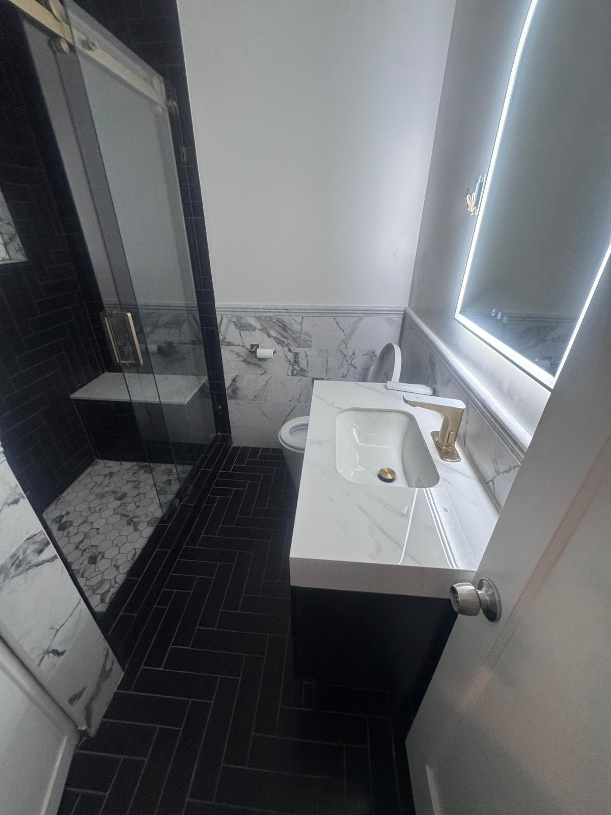 Black herringbone tile shower with white vanity and modern fixtures