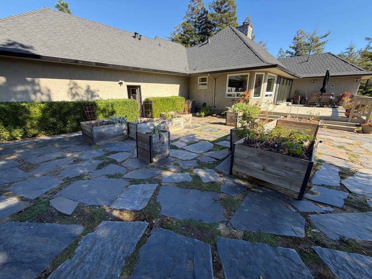 Backyard patio with slate stone flooring, black metal railings, and a single-story home with gray roof in the background