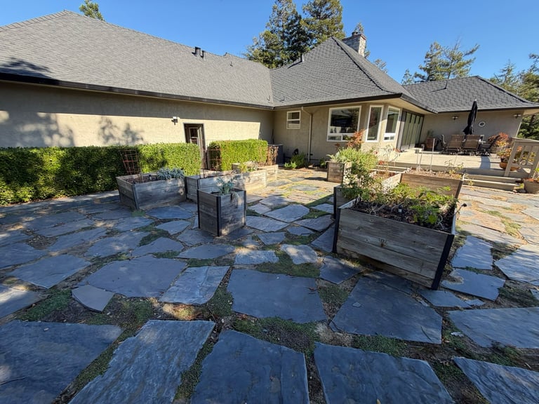 Residential backyard patio with slate stone flooring, black metal railings, and a single-story home with gray roof in the background