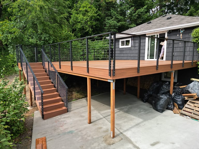 Side view of new elevated composite deck with black metal railing and matching staircase, attached to gray home