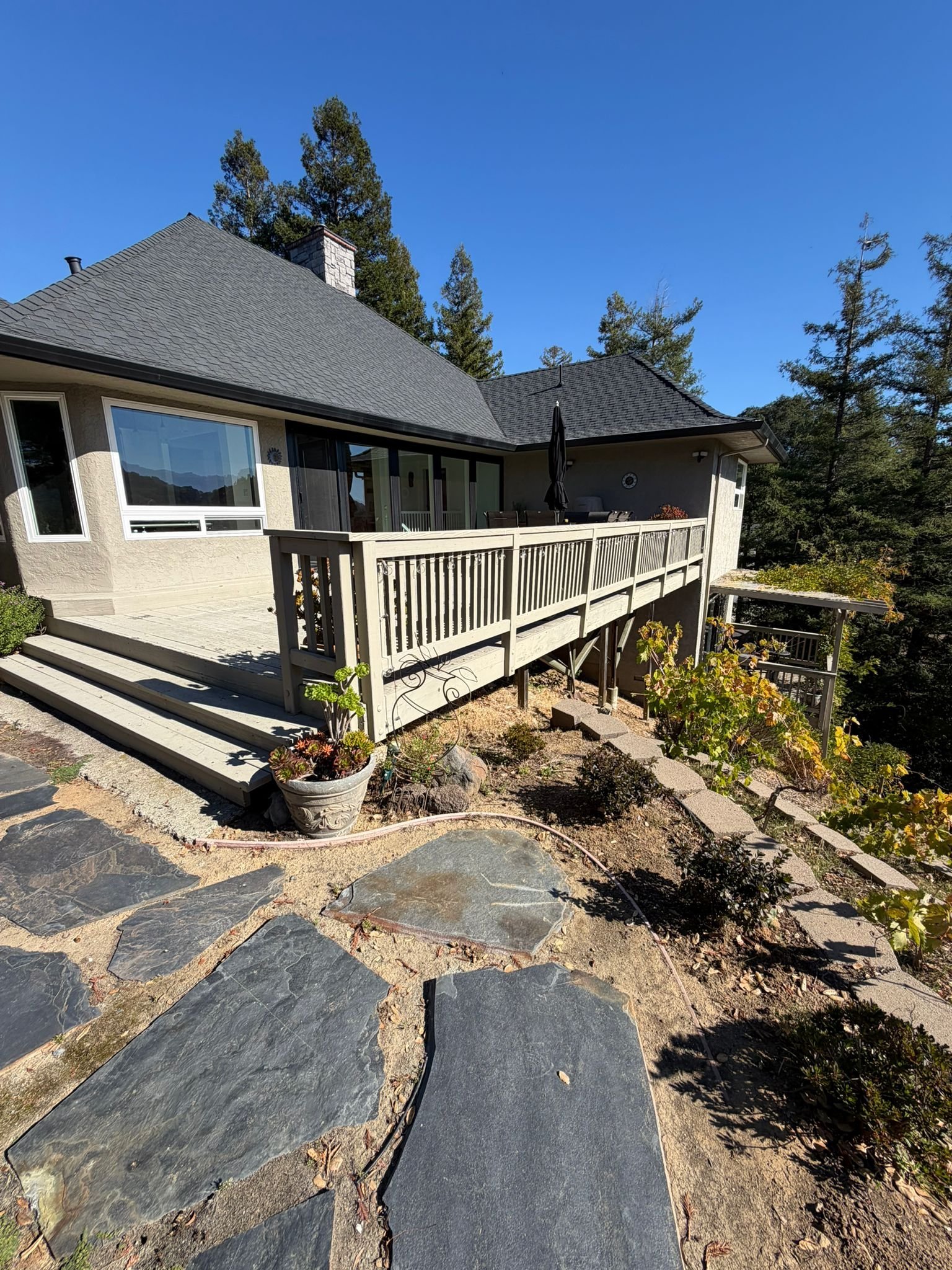 Cream and dark stone exterior with a white-railing entry and slate pathway surrounded by evergreen trees