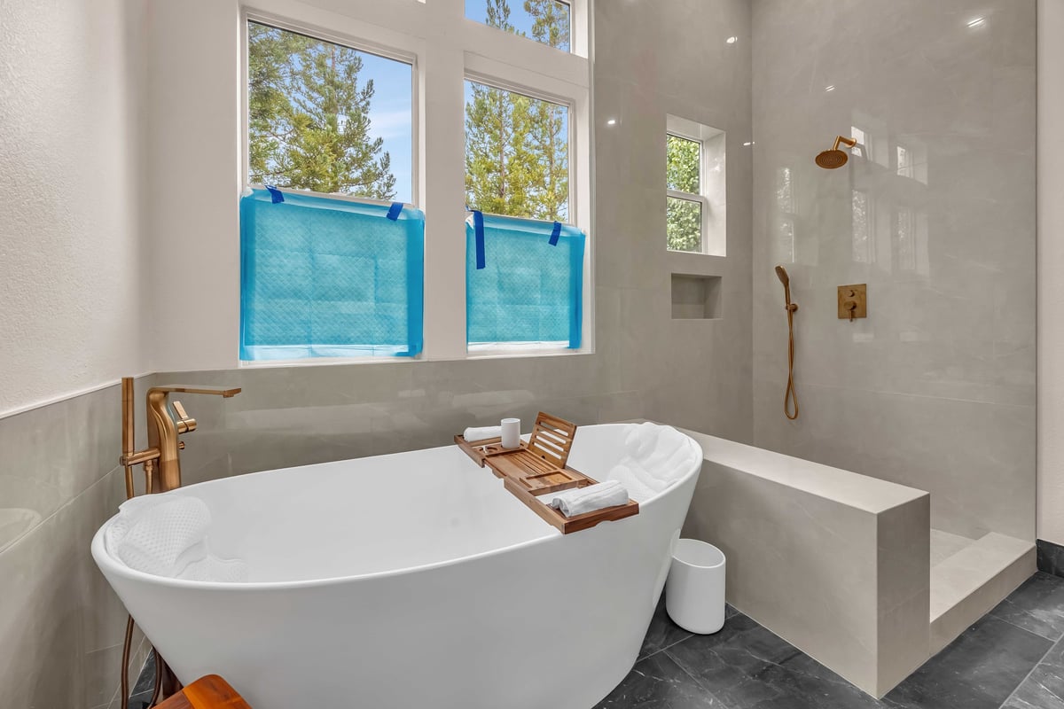 Luxury bathroom with freestanding bathtub, walk-in shower, and large windows overlooking redwoods