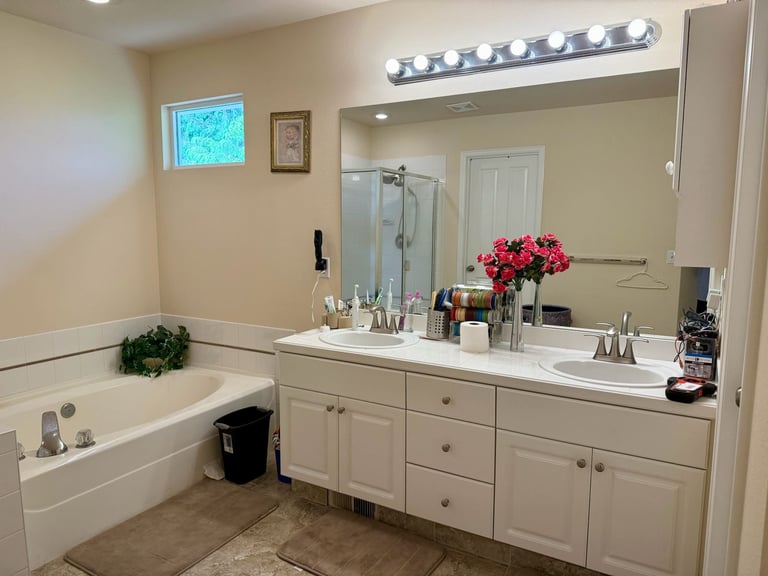 Modern bathroom with white vanity, large mirror with lights, white bathtub, and red flowers in vase
