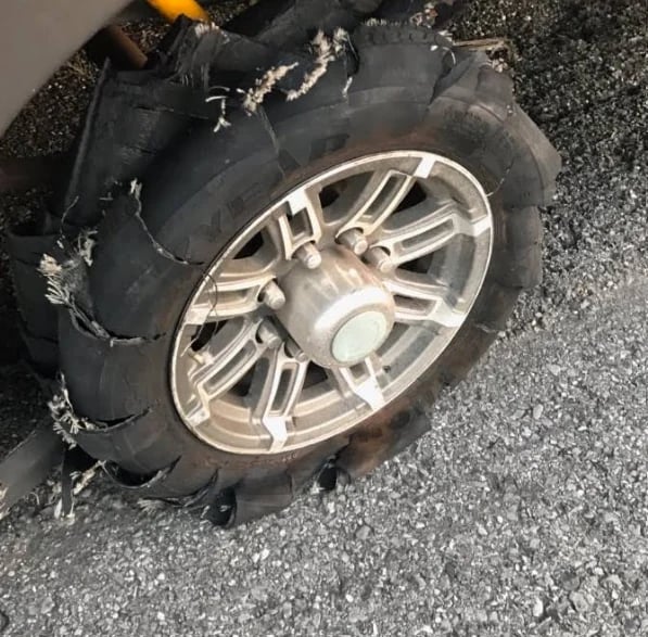 Damaged vehicle tire with shredded rubber and metal wheel rim exposed on asphalt