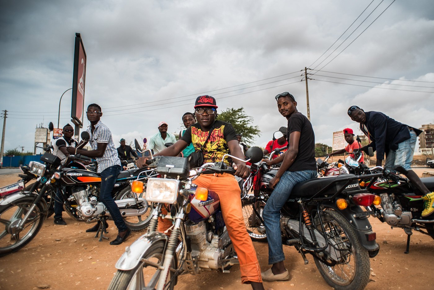 Group of men with motorcycles gathered outdoors on a dirt road under cloudy sky in an African setting