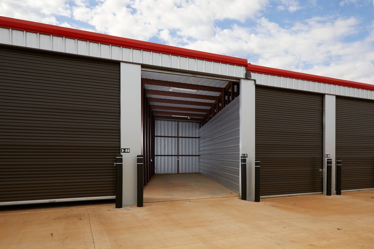 Modern Locked Up Self Storage units with red roofing and open garage doors, showing empty interior bays under clear blue sky