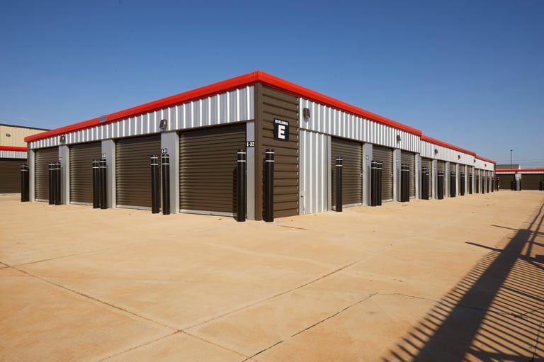 Row of industrial storage units with red roof and brown metal roll-up doors at Locked Up Self Storage