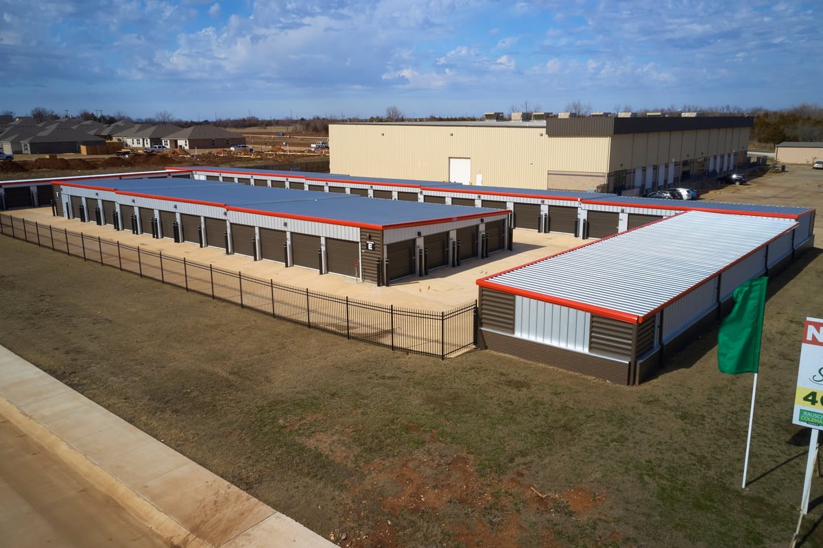 Aerial view of Locked Up Self Storage outdoor facility with blue and red roofed structures, surrounded by grass and fencing
