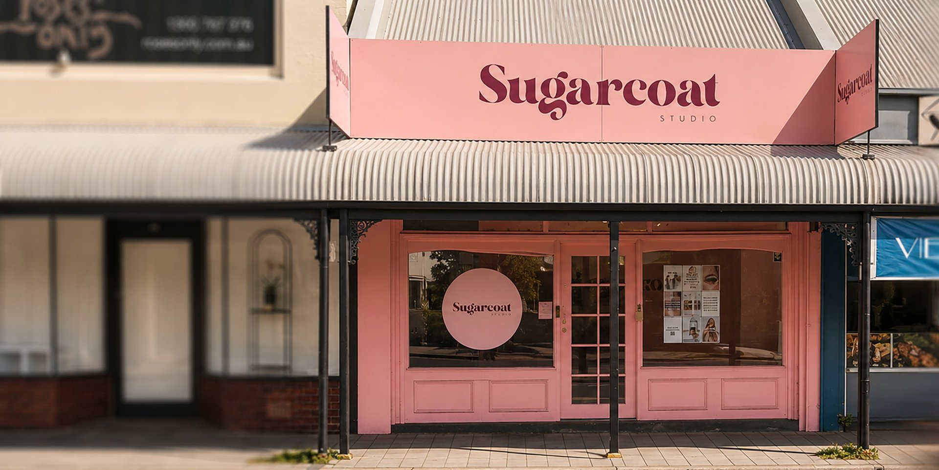 Pink storefront with Sugarcoat sign and double doors on a street with neighboring shops