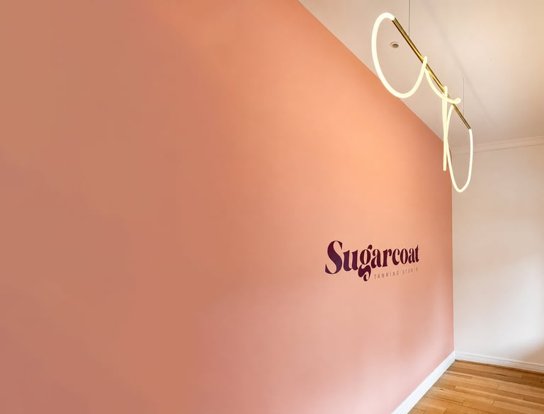 Modern interior with coral pink accent wall featuring Sugarcoat logo, white-framed mirror, and wooden flooring