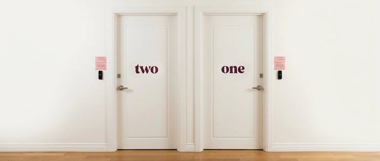 Two white doors labeled one and two with pink signs above them on a white wall with wooden flooring