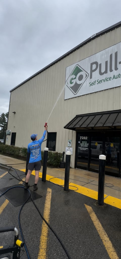 Person in blue shirt cleaning Go Pull self-service auto building sign with pressure washer