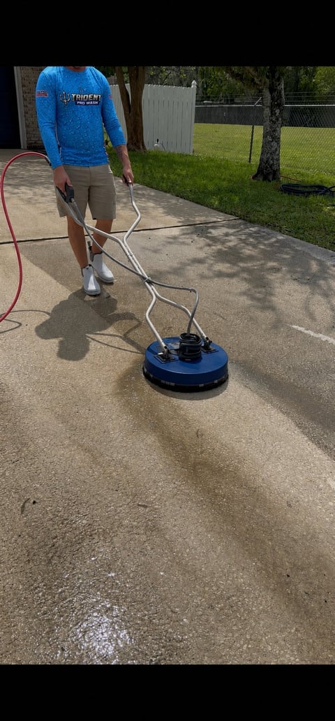 Person using a blue surface cleaning machine on a wet driveway in a residential backyard setting