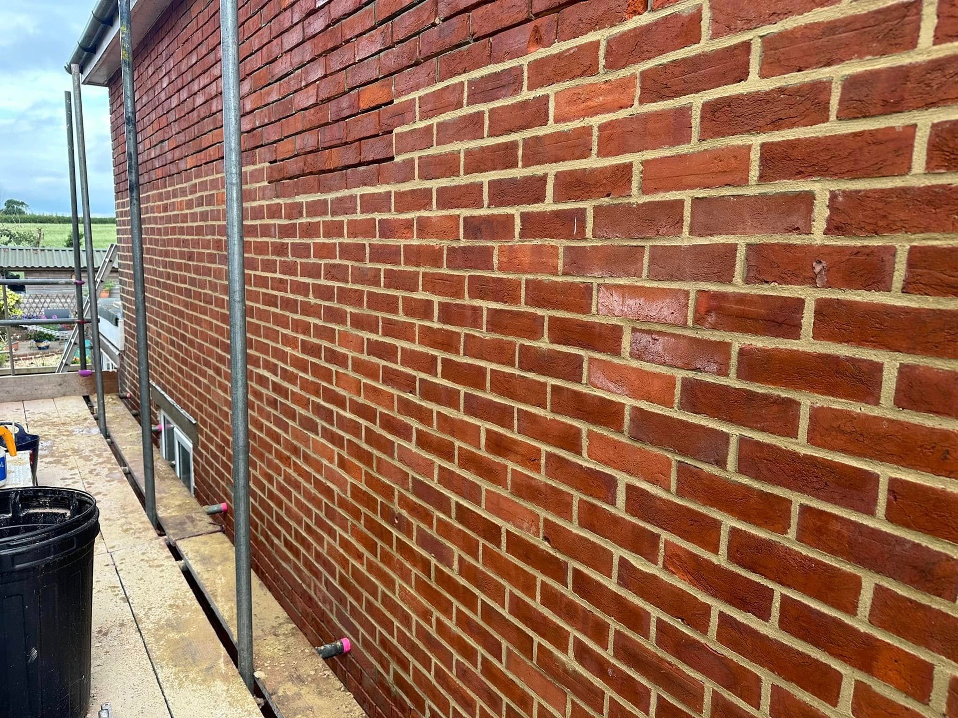 A red brick exterior wall of a building with weathered joints, alongside a metal downpipe