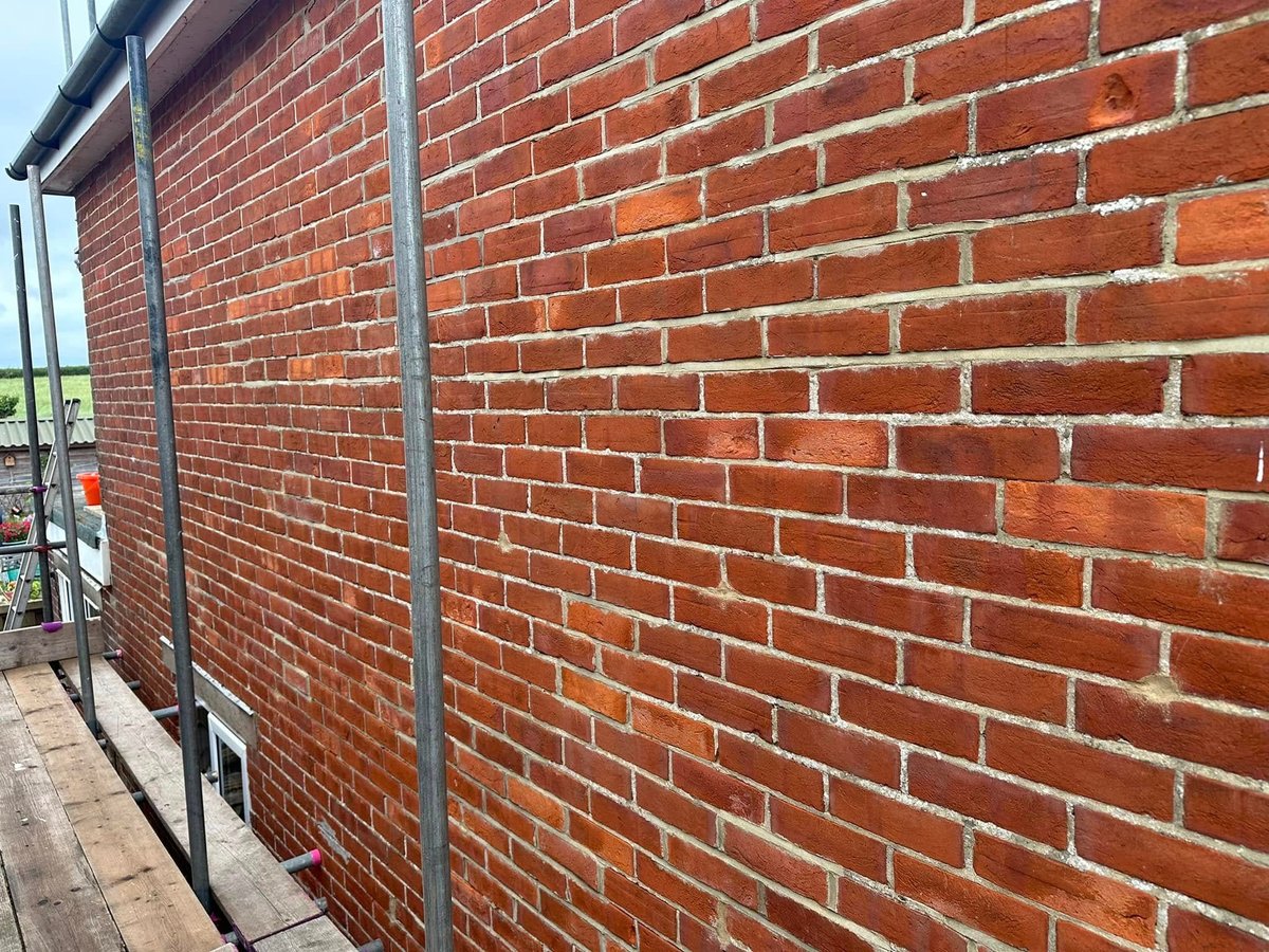 A red brick wall with metal guttering and downpipe alongside an outdoor concrete pathway