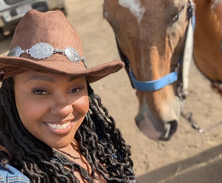 Shay, provider at Bear Cub Explorers, smiling next to a brown horse while wearing a tan cowboy hat