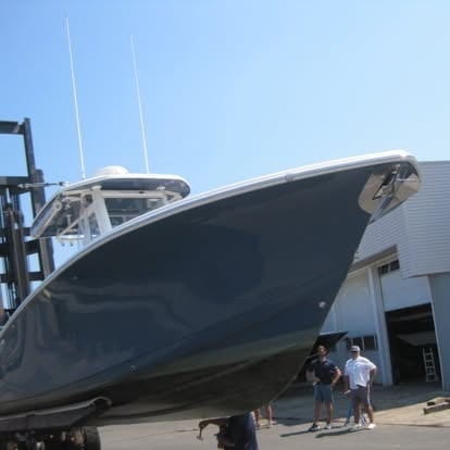 A large dark blue and white fishing boat on display at a shipyard with people viewing it from below