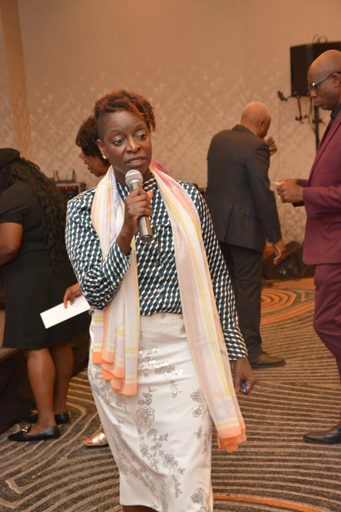Woman speaking at microphone at formal event wearing patterned jacket and scarf
