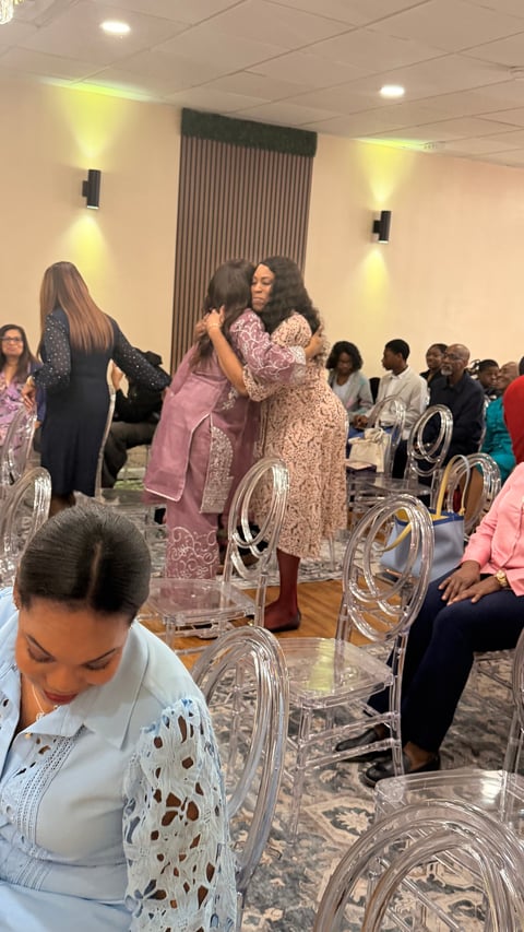 Women embracing at an indoor event in a banquet hall with clear chairs and warm lighting
