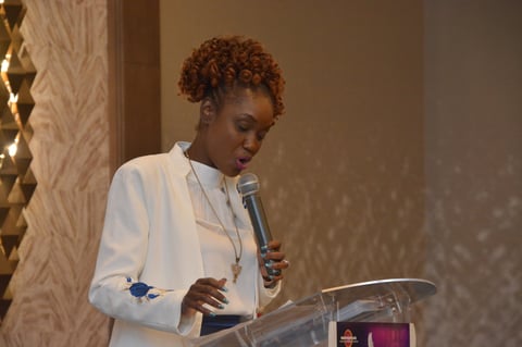 Woman with curly red hair in white blazer speaking at podium with microphone