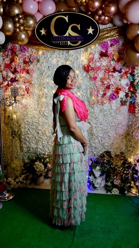 Woman in pink ruffled dress posing at elegant event backdrop with floral wall and CS logo sign